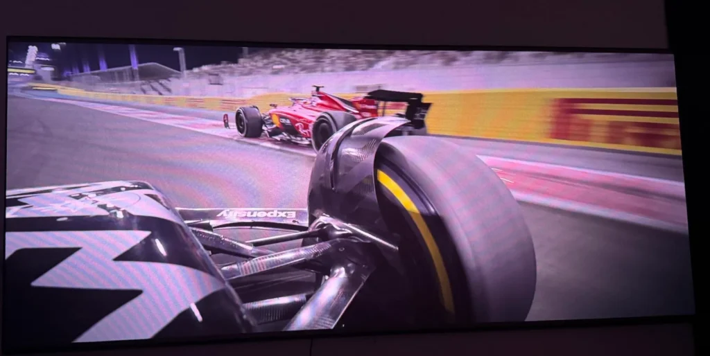 High-speed Formula 1 racing footage displayed on a large 4K projector screen. VisionMaster Max Gaming Performance Test