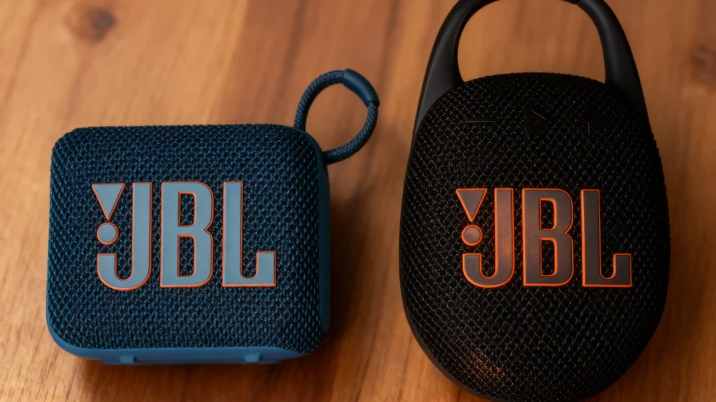 Teal JBL Go 4 and black JBL Clip 5 speakers side-by-side on wood.