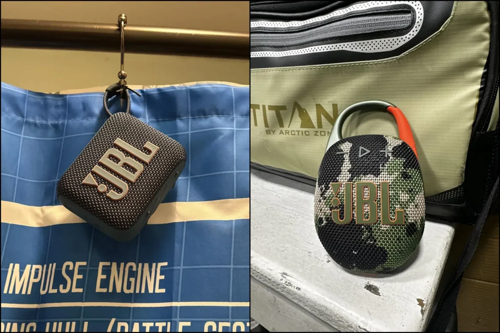 Black JBL Go 4 hanging from a hook and camouflage JBL Clip 5 on a bag.