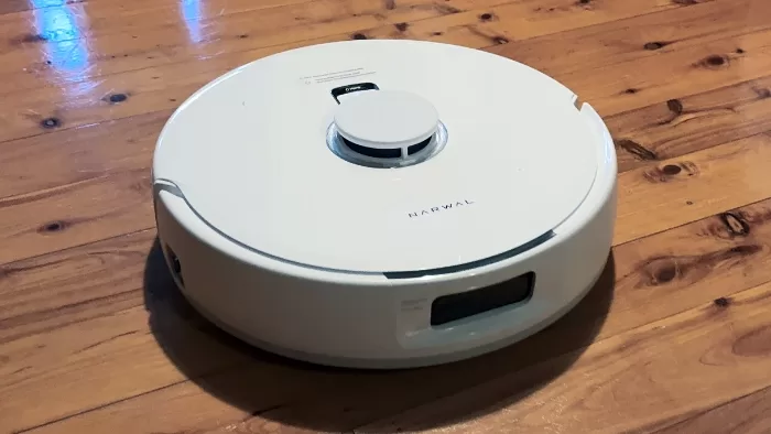 Black Roborock Q5 Max+ robot vacuum cleaning pet hair on a brown carpet near a white cat.