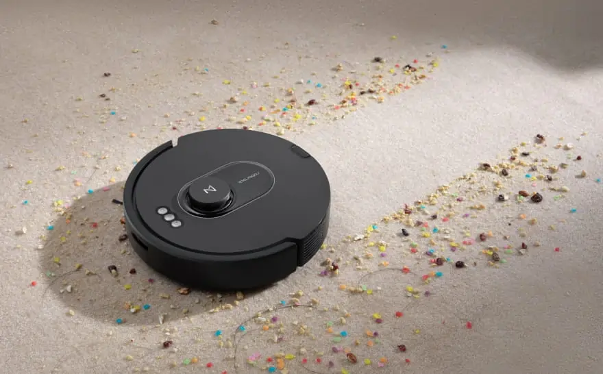 Roborock Q5 Max+ robot vacuum cleaner cleaning colorful debris on a light-colored carpet.